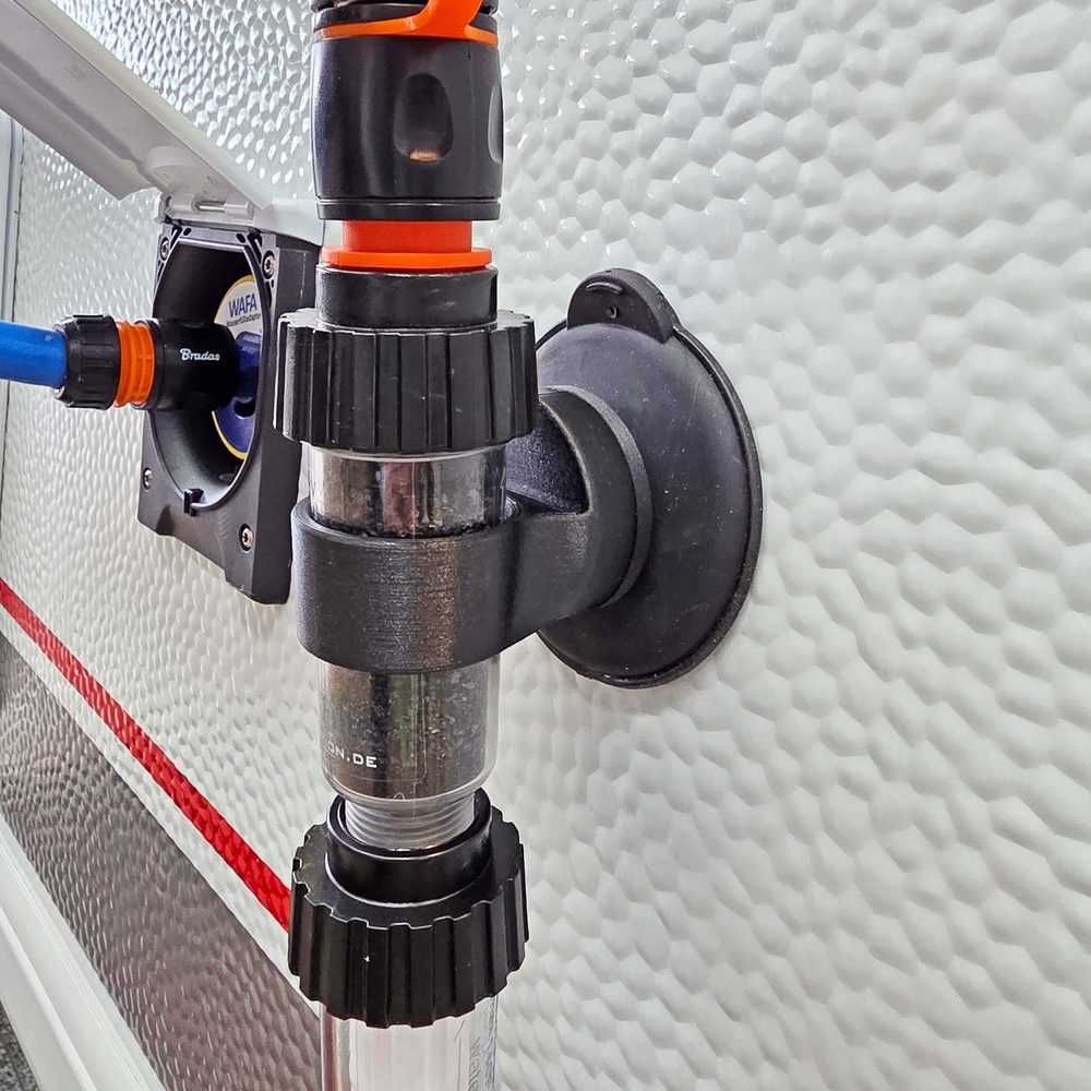 CamperFilter mit ClingCup-Halter an einer Wohnwagenwand mit Hammerschlag-Oberfläche, daneben der Einfüllstutzen